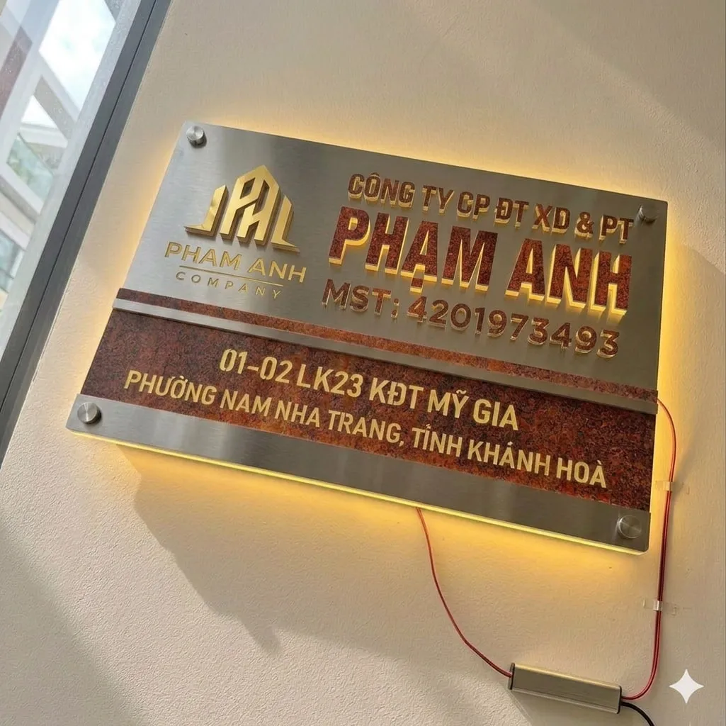 Bảng hiệu công ty inox giả đá LED halo gắn tường sáng đèn ban đêm – phối cảnh thực tế Bảng hiệu công ty inox giả đá LED halo vàng ấm chữ nổi 3D gắn tường văn phòng sáng ban đêm
