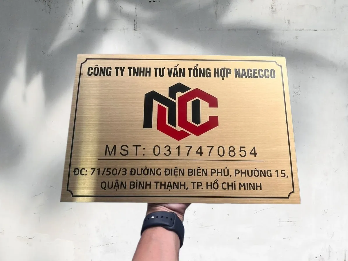 Bảng hiệu công ty inox vàng xước — phối cảnh thực tế khi cầm trên tay Phối cảnh thực tế bảng hiệu công ty inox 304 vàng xước chữ ăn mòn sơn tĩnh điện đỏ đen khung viền — hoàn thiện sẵn sàng lắp đặt