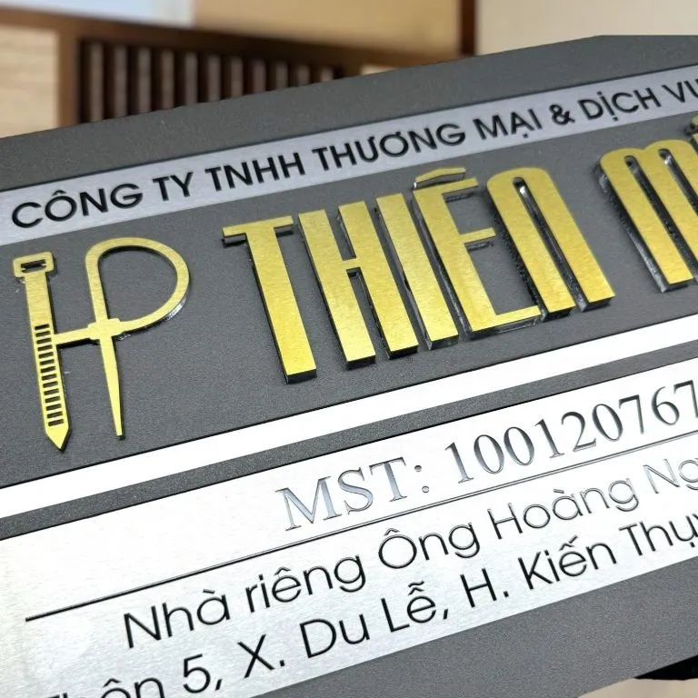 Cận cảnh chữ nổi 3D inox vàng xước và logo dựng inox trên bảng hiệu công ty xám khói bạc 2 lớp