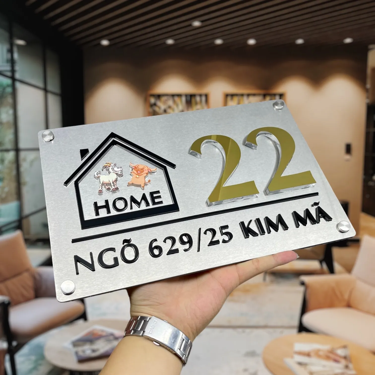 Họa tiết ngôi nhà viền đen và nhân vật hoạt hình trên bảng số nhà inox vàng gương