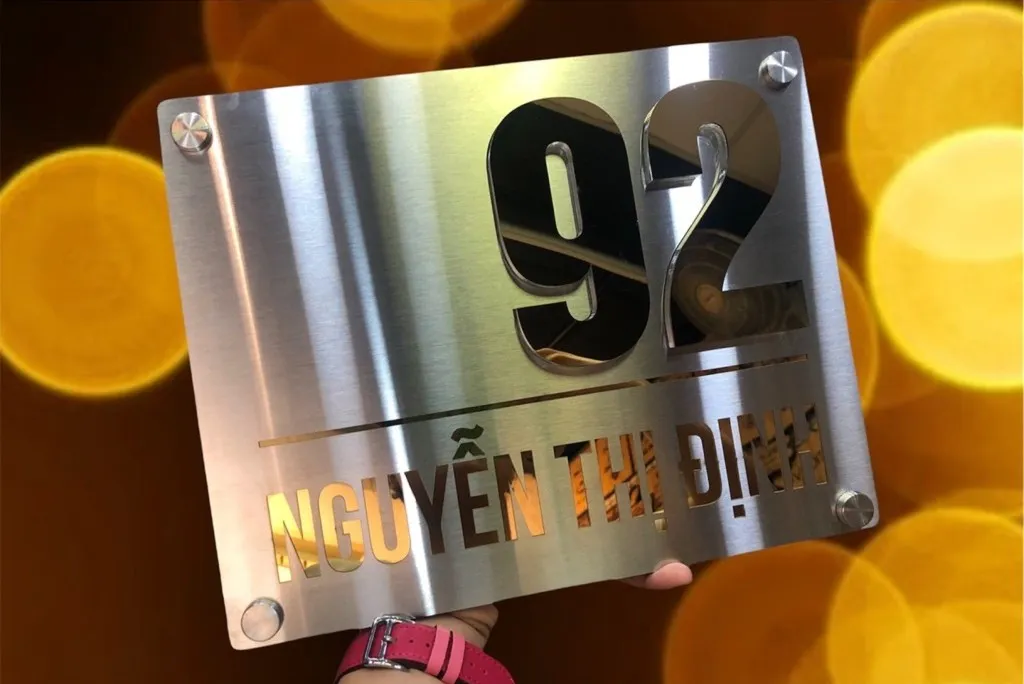 Bảng số nhà inox xước bạc chữ số vàng gương nổi 3D chụp nghệ thuật với bokeh ánh sáng vàng lung linh phía sau