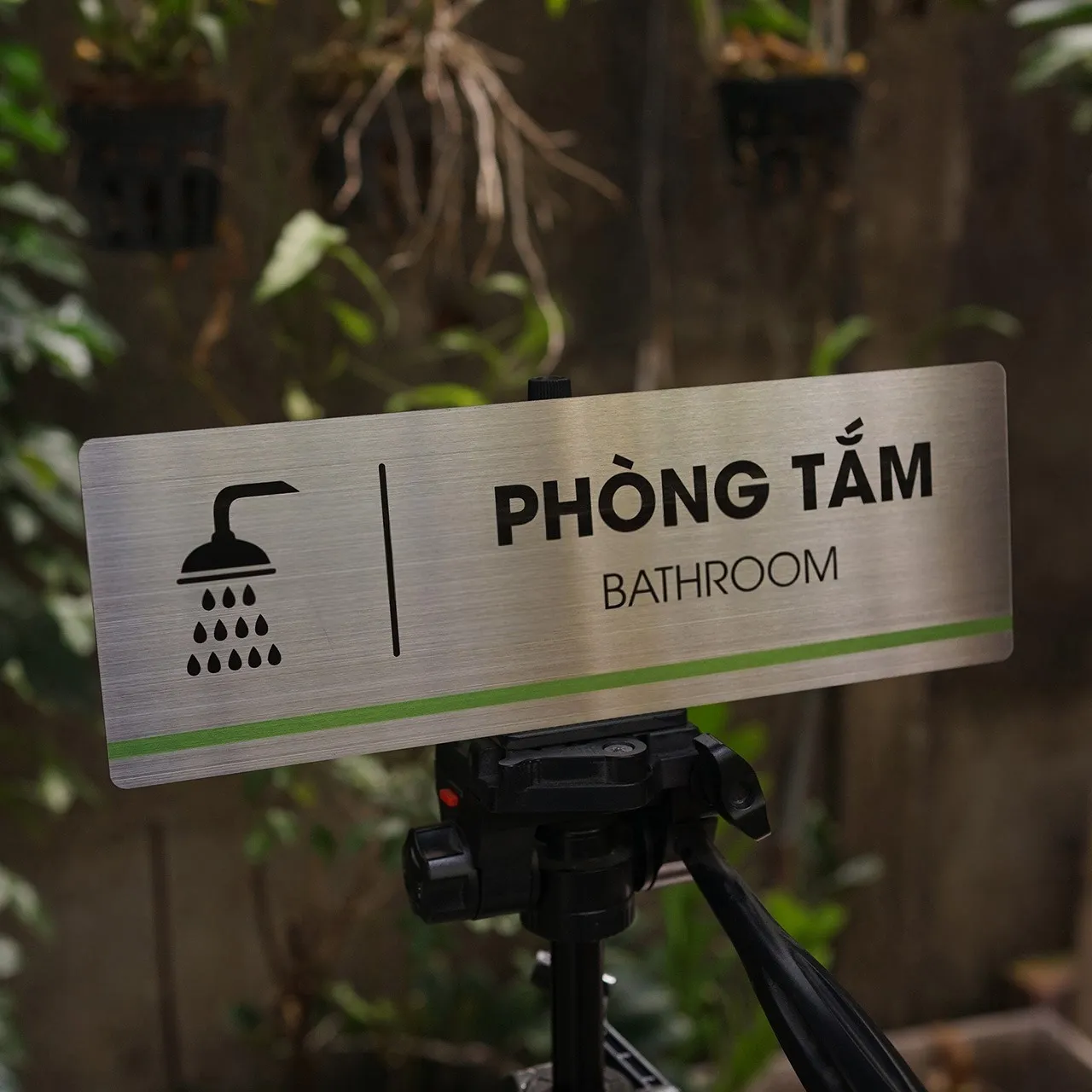 Bảng tên phòng tắm inox 304 phay xước góc chụp thấp trên tripod nền tường gỗ