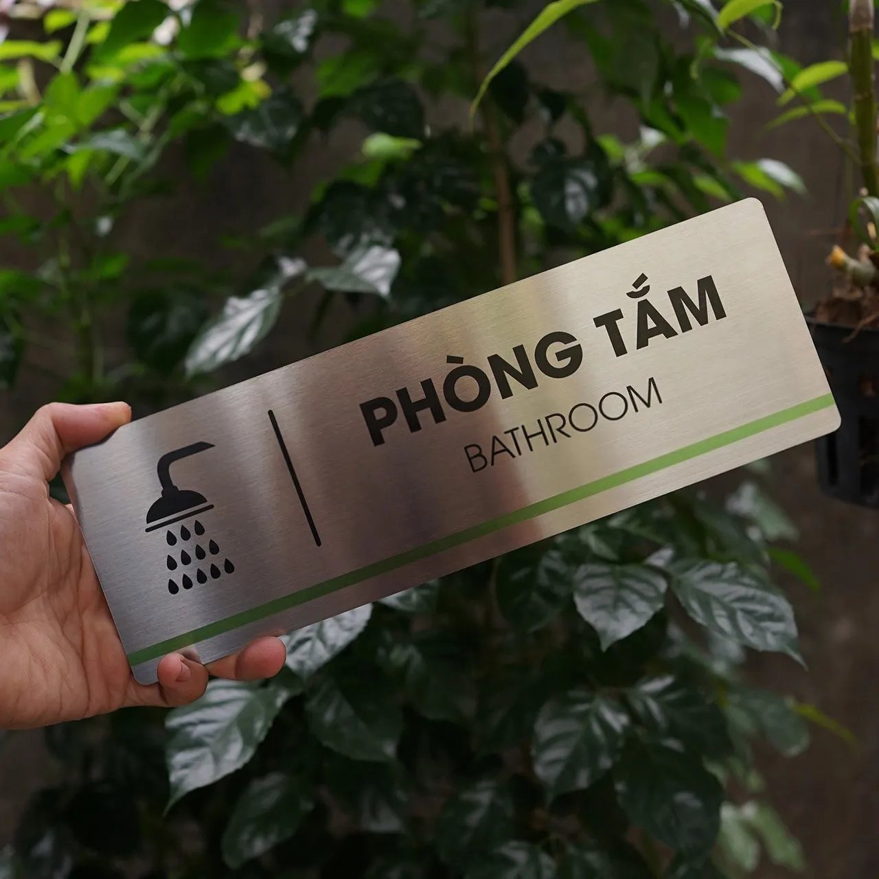 Bảng tên phòng tắm inox 304 cầm tay góc nghiêng nhẹ thấy rõ bề mặt phay xước và sọc xanh lá