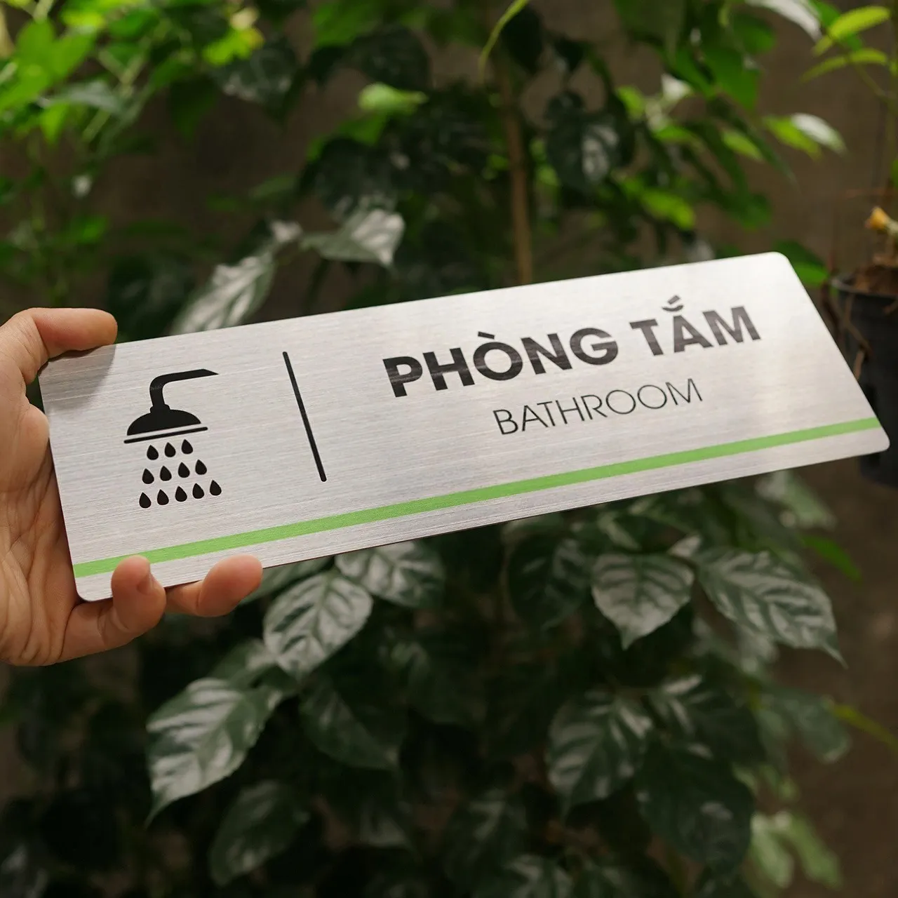 Bảng tên phòng tắm inox 304 phay xước cầm tay toàn cảnh mặt trước nền cây xanh tối