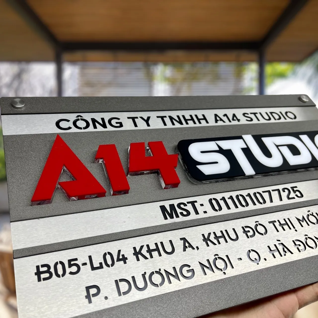 Toàn cảnh bảng hiệu công ty inox 2 lớp xám khói xước bạc chữ nổi 3D đa màu cầm tay phối cảnh không gian mở ngoài trời
