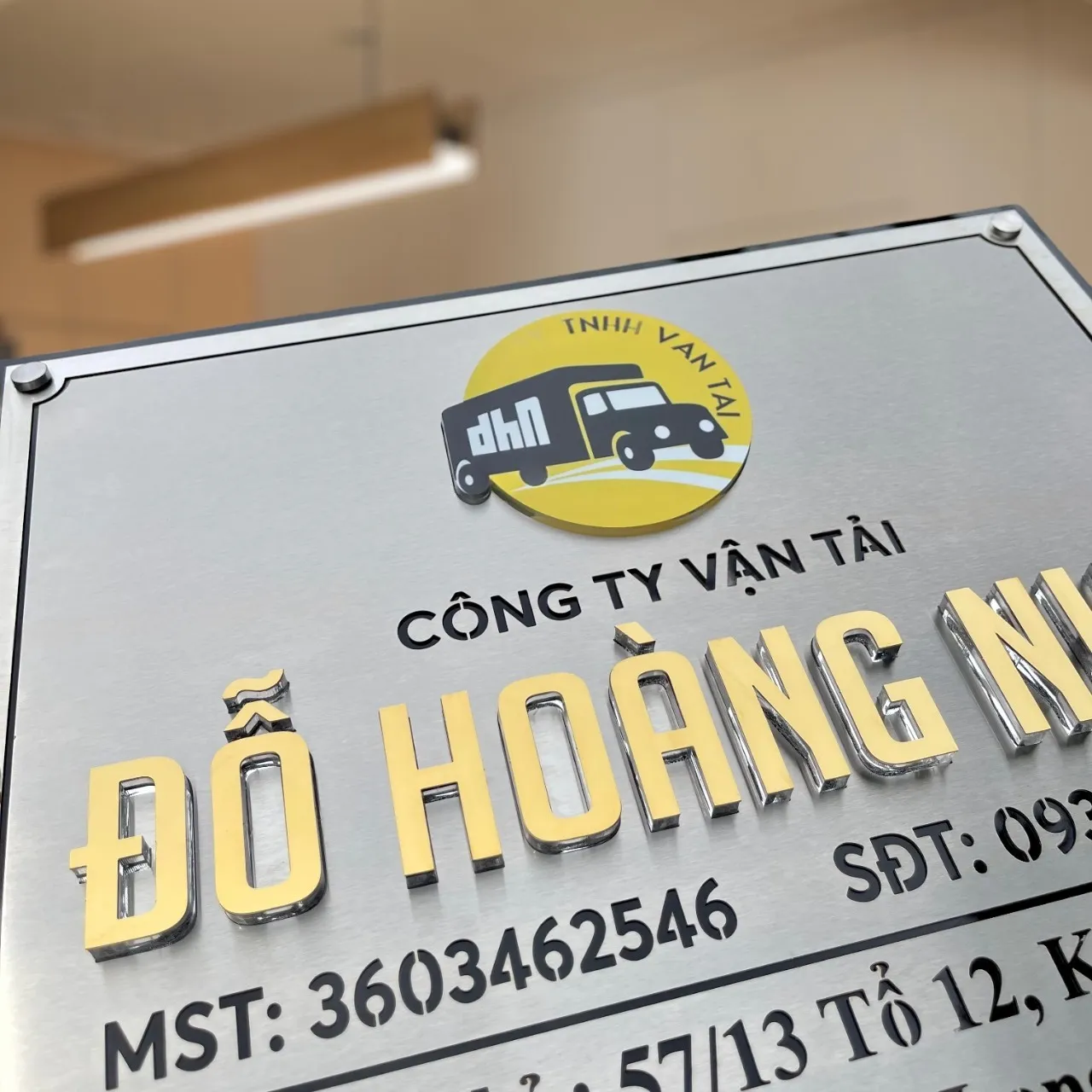 Cận cảnh chữ nổi 3D vàng gương và logo công ty trên bảng hiệu inox 304 xước bạc Cận cảnh chữ nổi 3D inox vàng gương dày 15mm và logo công ty vận tải in UV đính nổi trên bảng hiệu inox xước bạc