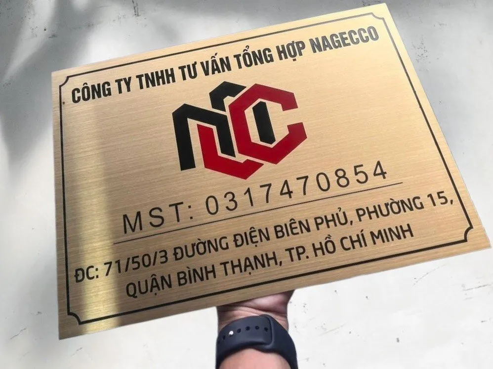 Bảng hiệu công ty inox vàng xước nhìn từ góc nghiêng 45 độ — chiều sâu và ánh sáng Bảng hiệu công ty inox 304 vàng xước nhìn từ góc nghiêng 45 độ, thể hiện độ dày 15mm và hiệu ứng ánh kim