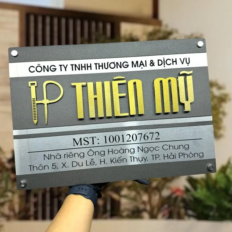 Bảng hiệu công ty inox xám khói bạc 2 lớp chữ nổi vàng logo tùy chỉnh phối cảnh cầm tay trước nhà phố