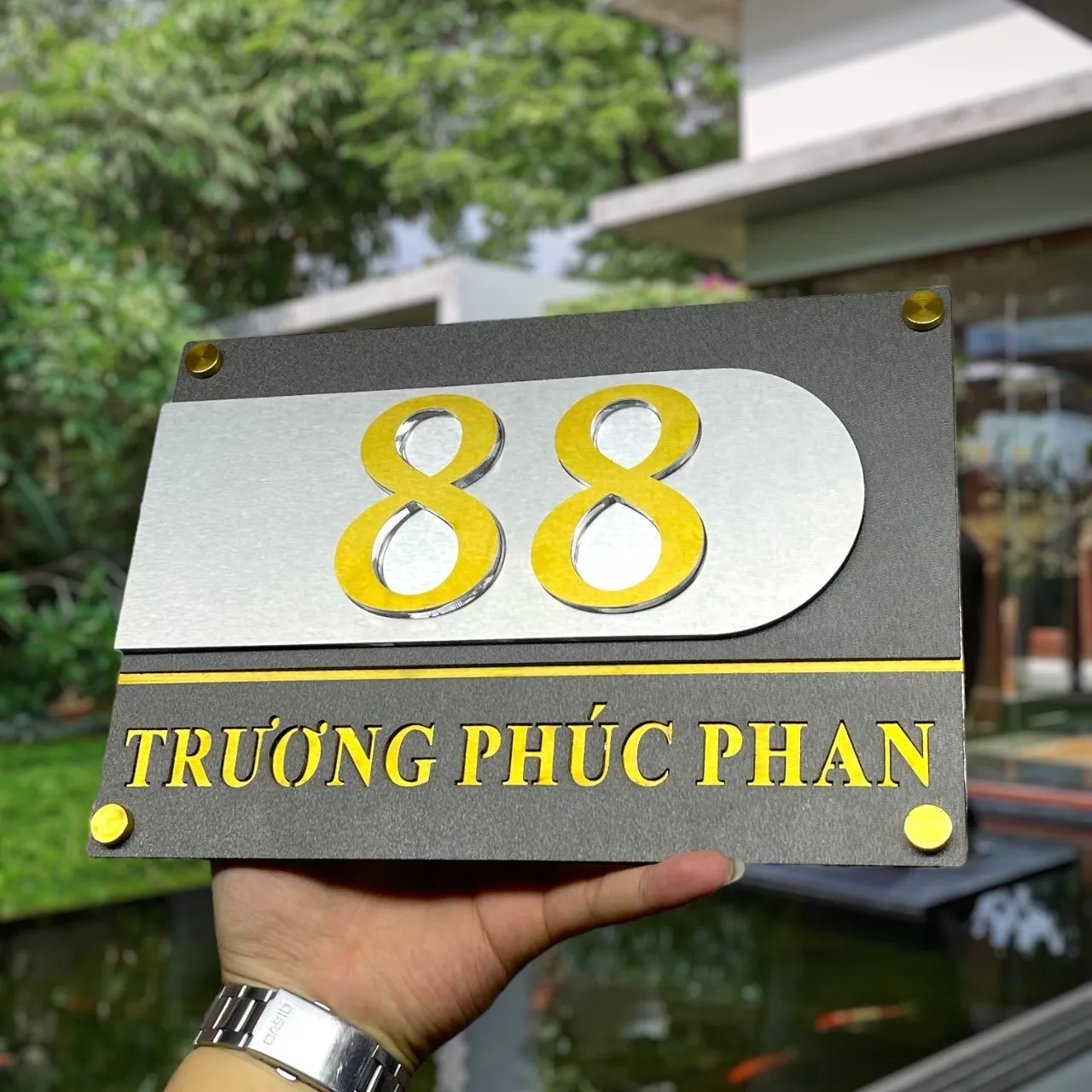 Bảng số nhà inox 2 lớp chữ vàng gương nền xám khói phối cảnh thực tế ngoài trời hồ cá