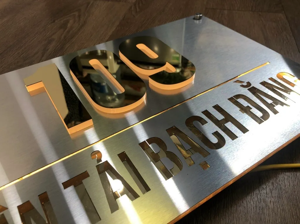 Chi tiết chữ số inox vàng gương nổi 3D với đèn LED viền sáng halo phía sau trên nền inox bạc xước
