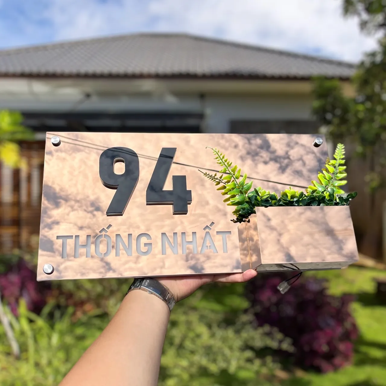 Bảng số nhà inox vàng gương tích hợp chậu cây phối cảnh ngoài trời ban ngày trước cổng nhà vườn