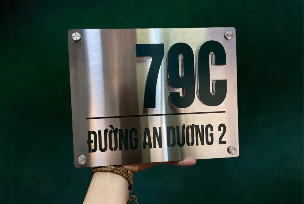 Bảng số nhà inox xước bạc chữ số đen nổi 3D đặt trên nền xanh lá – màu bạc xước nổi bật tương phản với nền tối