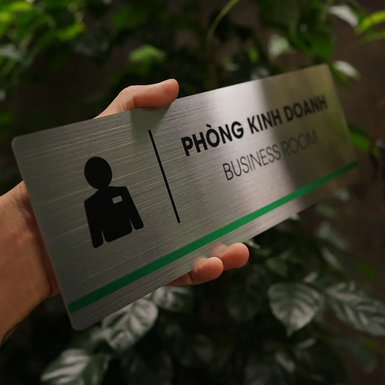 Bảng tên phòng kinh doanh inox 304 cầm tay nhìn từ góc cao thấy rõ vân phay xước phản sáng và góc bo tròn